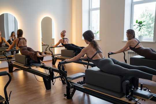 Fitness instructors performing pilates exercises using reformer beds and resistance bands, promoting healthy lifestyle and core strengthening - Powered by Adobe