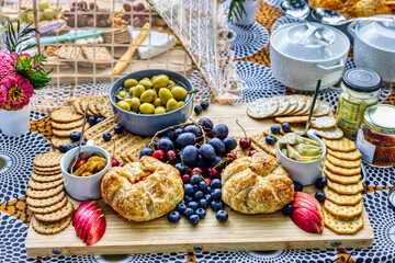 grazing board ,charcuterie board at an outdoor gathering. The board is filled with various snacks, including crackers, grapes, olives, and bread rolls,