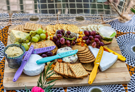 cheese board, cheese platter at an outdoor gathering , appetizer or a course featuring a variety of cheeses The board is filled with various snacks, including crackers, grapes,