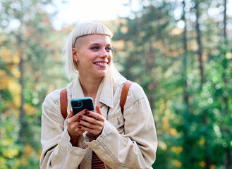 Hiking woman enjoys nature with trekking poles using navigation app on her mobile phone in a lush forest during a sunny day