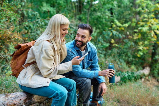 Hiking couple enjoys nature using navigation app on her mobile phone and taking a break with water bottle in a lush forest during a sunny day