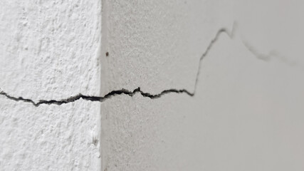Obraz premium Close-up of a distinct diagonal crack in the corner of a rough white painted concrete or stucco wal, showing damage and decay.
