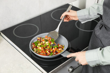 Woman stirring mix of fresh vegetables with slotted spatula in frying pan, closeup