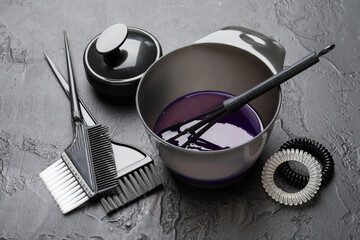 Hair dyeing product in bowl and different hairdresser's tools on black table, closeup
