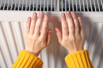 Woman warming her hands near radiator indoors, closeup