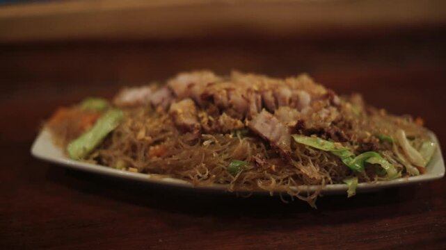 Traditional Filipino stir-fried noodles with meat and vegetables served in Bohol, Philippines Close-up of pancit bihon with pork slices and mixed vegetables on a plate in Bohol, Philippines