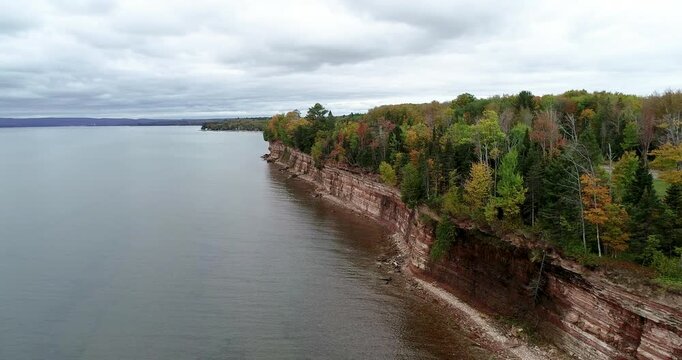 Aerial 4K drone footage flying right to left along sandstone cliffs and fall foliage at Baraga Cliff Roadside Park overlooking Keweenaw Bay, Michigan