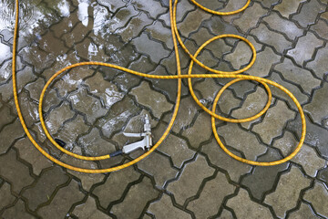Yellow garden hose with nozzle coiled messily on wet pavement. This backyard ground tool for watering creates simple background, evoking sense of calm after work