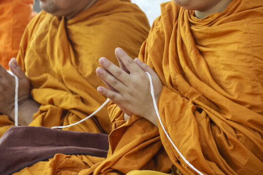 Serene Buddhist monk with hand in pray gesture, wearing an orange robe during spiritual ceremony in temple. moment of faith, religion, tradition, and peace
