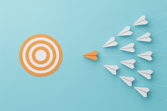 Leadership and goal alignment concept with orange paper plane guiding team to target on blue background.