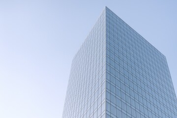 Fototapeta premium Modern Glass Skyscraper Reaching into Pale Blue Sky, Minimalist Architecture for Business and Finance