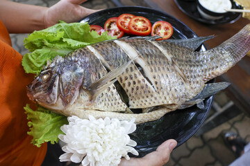 Appetizing grilled whole fish dinner on black plate. delicious meal of fresh tilapia served with tomato and lettuce garnish, representing healthy culinary food concept