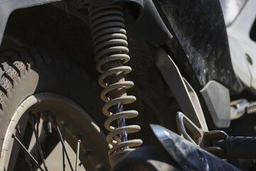 Close up detail of dirty motorcycle shock absorber part. muddy suspension spring and wheel show...