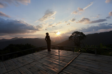 Lone traveler silhouette standing on wooden viewpoint enjoys peaceful mountain sunset. serene...