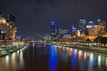 Yarra River, Melbourne CBD, Australia, Wide night cityscape view of the CBD skyline and Flinders Street Station, with strong illumination reflecting on the calm water of the Yarra River.