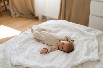 Cute baby lying on a soft white blanket with a calm expression while raising arms. Beautiful portrait of a child. Newborn baby lying on bed