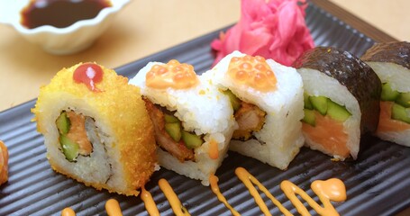 Assorted Sushi Rolls on a Black Plate with Soy Sauce and Pickled Ginger