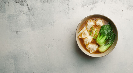 Wonton soup with bok choy in dark bowl on light background, top view, copy space