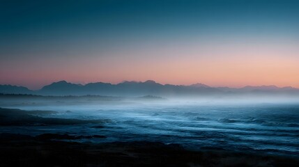 Obraz premium Misty ocean coastline at dawn with distant mountains and a serene gradient sky