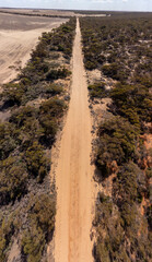 Aerial view of a long, straight sandy road cutting through the dry Mallee landscape near Walpeup, Victoria, bordered by native scrub and farmland under a bright sky. 