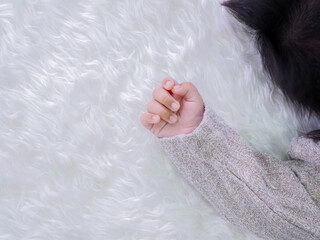 Close up of newborn baby hand is wearing a grey sweater on white rugs