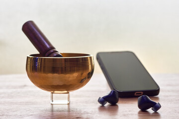 Tibetan singing bowl with smartphone and wireless earbuds for guided meditation app.