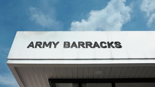 Army barracks word sign displayed on a solid, uniform-style building beneath a clear blue sky, conveying structure, discipline, order, security, and an organized living environment for soldiers