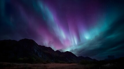 Naklejka premium Vibrant Aurora Borealis illuminates a dark mountainous landscape under a star filled night sky
