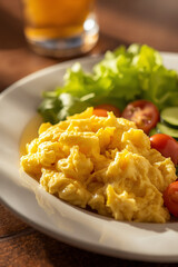 Macro shot of scrambled eggs served with fresh salad on white ceramic plate. Warm daylight, shallow focus, and balanced shadows add freshness and warmth perfect for culinary promotion.