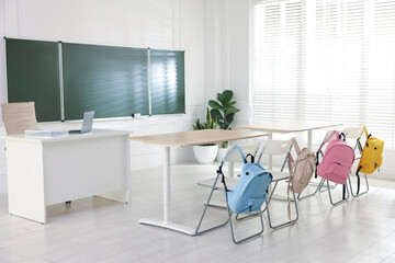 Green chalkboard, backpacks and stylish furniture in classroom. Mockup for design