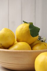 Fresh ripe quinces with leaves in bowl on table, closeup