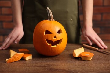 Halloween celebration. Woman with carved pumpkin at wooden table against brick wall, closeup
