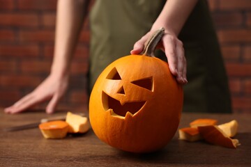 Halloween celebration. Woman with carved pumpkin at wooden table against brick wall, closeup