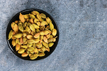 Dried cardamom seeds in bowl on stone background, top view