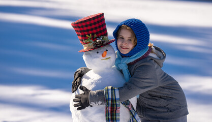 Kid building a snowman on winter day. Childhood and winter fun. Kid creating snowman outdoors. Kid enjoying snow winter fun and making snowman. Kid playing with snowman. Winter kids face.