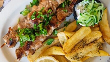 Indulge in a delicious Greek souvlaki plate with tender grilled meat skewers, crispy french fries, refreshing tzatziki sauce, and a zesty lemon wedge to elevate the flavors.