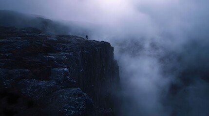 A lone figure stands at the precipice of a dramatic mist shrouded cliff contemplating the vast moody landscape at dawn