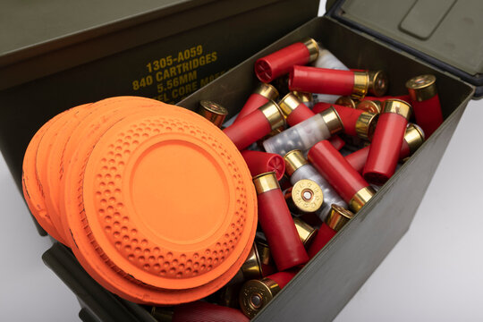 Flying clay target and bullet shotgun shell in green army ammo crate on white background