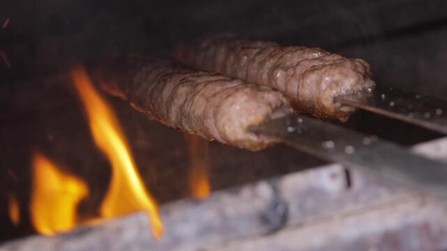 Skewer kebab roasting over open flame inside charcoal oven, meat browning and juices dripping into embers, rustic streetfood or restaurant grill scene filled with smoky