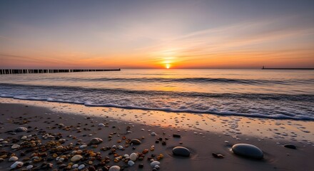 Calm beach scene with a vibrant sunset over the ocean and rocks on the sand near the water line