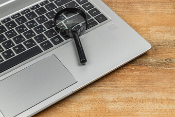 Magnifying glass resting on a silver laptop keyboard on wooden table