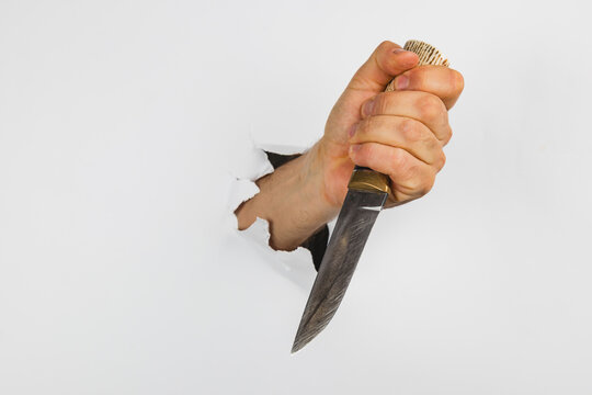 Hand holding a knife breaking through a white wall