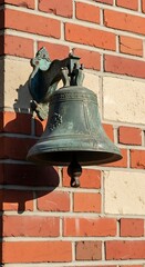 Fototapeta premium Antique bronze bell mounted on a brick wall, casting a shadow.
