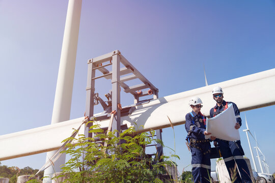 An engineer carefully examines a wind turbine blade at a construction site, placing a large blade on the ground to highlight the renewable energy technology.