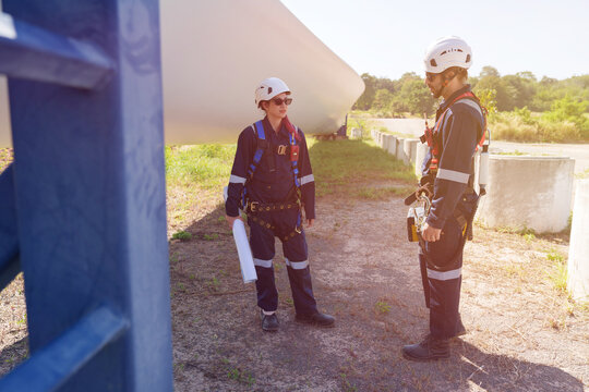 An engineer carefully examines a wind turbine blade at a construction site, placing a large blade on the ground to highlight the renewable energy technology.