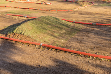 Dirt Track Obstacle Course with Red Hoses and Grass Mound under Sunlight on Rugged Earth Terrain