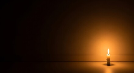 A lone candle flickers in the darkness casting a soft warm glow on the surface and the wall behind it