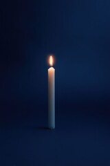 Fototapeta premium Illuminated candle stands alone against deep blue backdrop, symbolizing hope