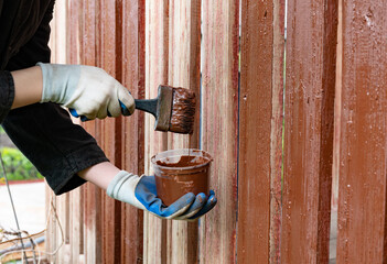 Painting wooden fence with brown paint during daytime