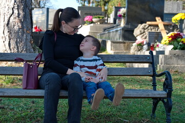 Mother and her little boy sitting on the bench in a cemetery